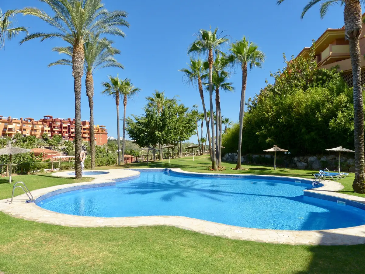 Piscina rodeada de jardines y palmeras en La Reserva de Marbella